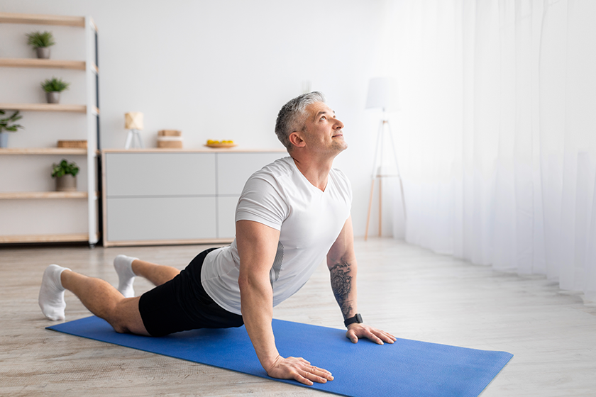 Active senior man doing cobra pose on yoga mat