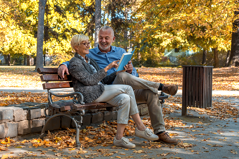 elderly-couple-sitting-bench-reading-book-park